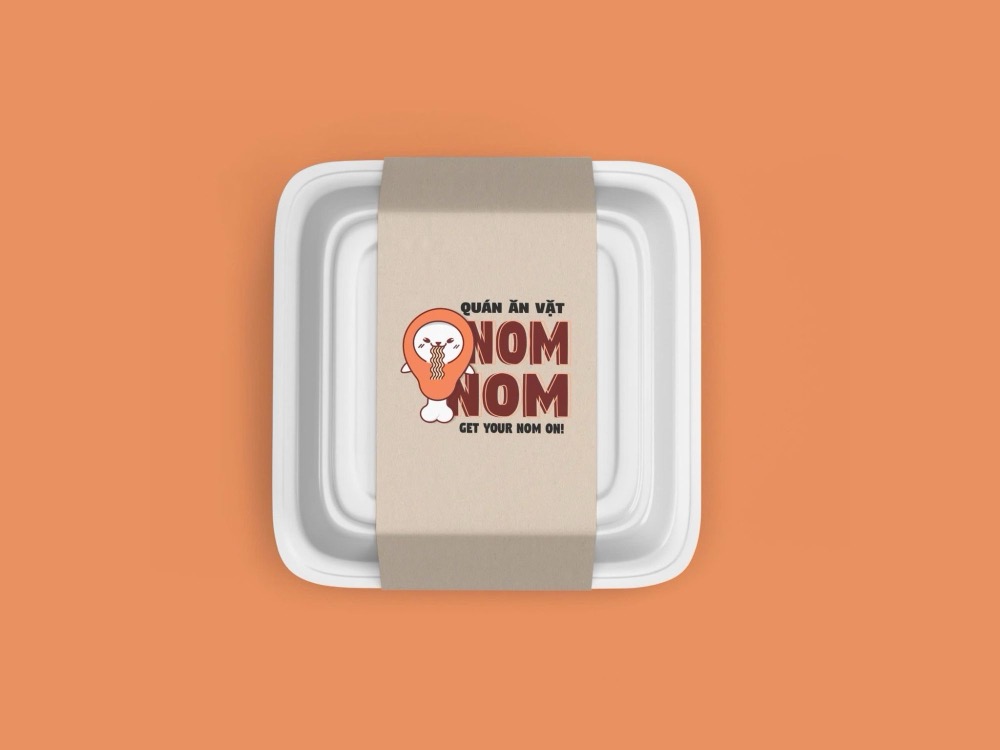 Tem đai giấy kraft quanh khay đựng đồ ăn với logo NOM NOM, linh vật đùi gà hút mì, dòng Quán ăn vặt và slogan GET YOUR NOM ON!